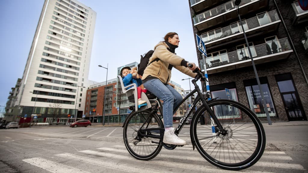 En kvinna cyklar längs en gata bredvid en hög byggnad