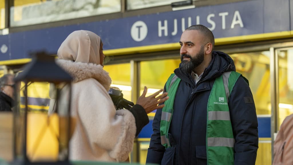 En man i huvjacka pratar med en kvinna.