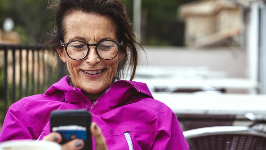 Äldre kvinna sitter tittar på sin mobiltelefon.