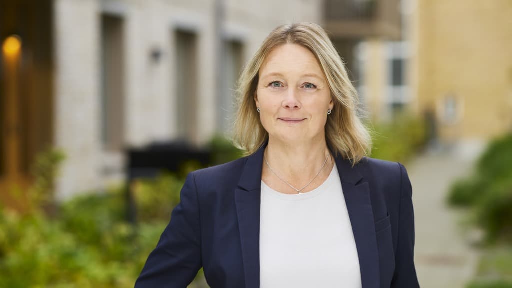 Karin Jacobsson framför ett hus med ljus fasad och gröna rabatter.