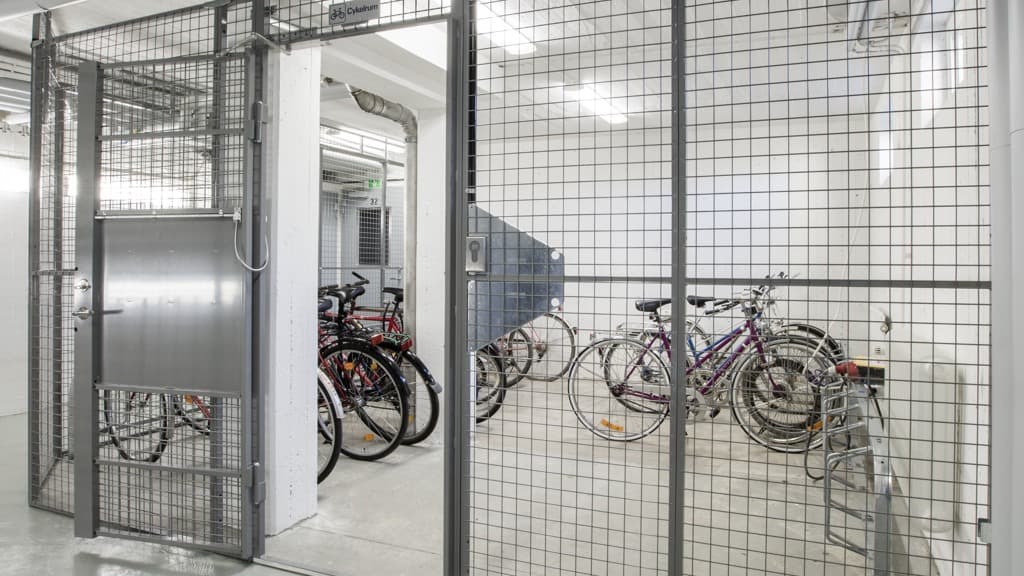 Ett cykelrum med väggar av stålgaller.  Cyklar i cykelställ i rummet.