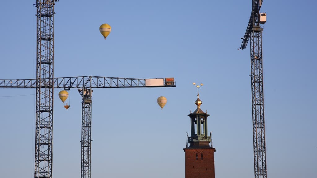 Stockholms stadshus med lyftkranar och luftballonger i bakgrunden.