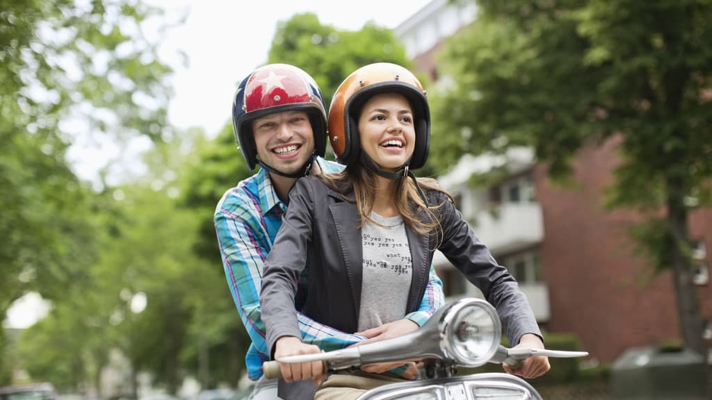 Ett ungt par som åker tillsammans på en moped.