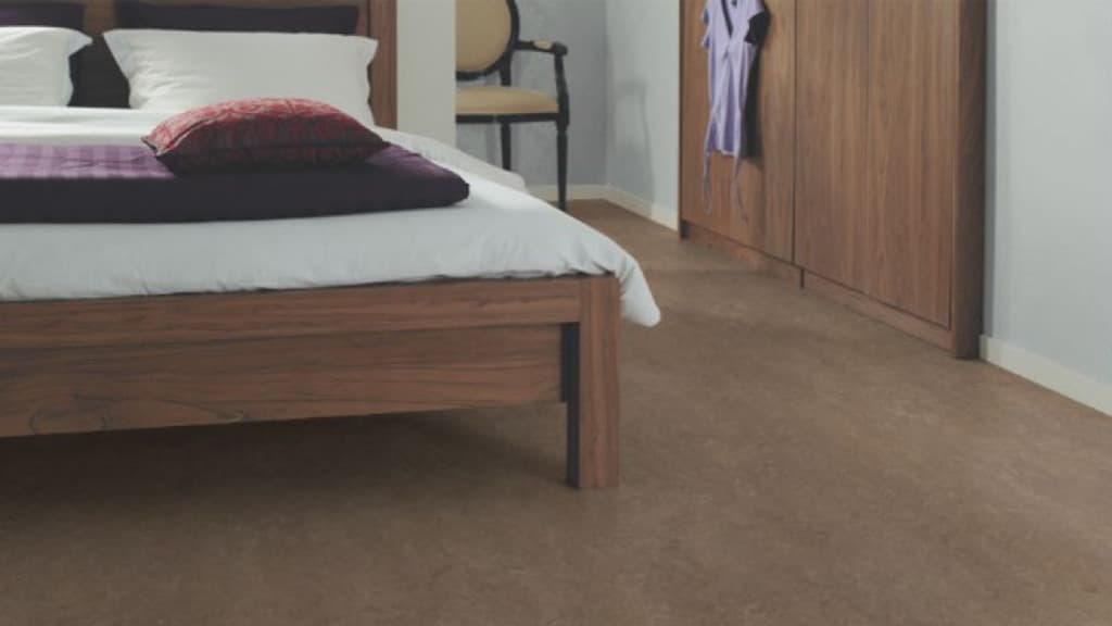 Ett sovrum med dubbelsäng och garderob i trä och ljusa väggar. Beige linoleum på golvet.