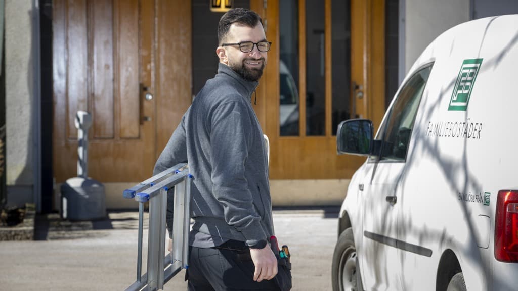 Husvärd i arbetskläder med stege under armen som vänder sig om bredvid en skåpbil med FB-logga