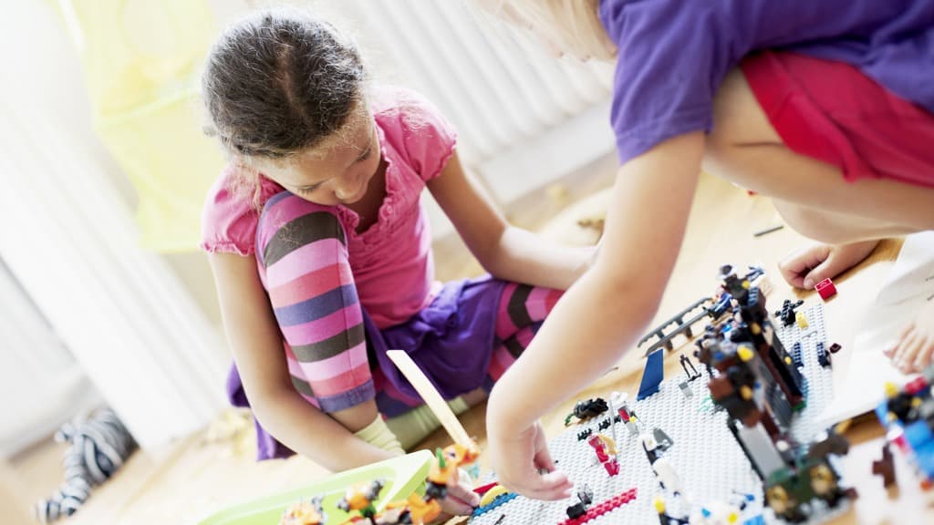 Två flickor i färgglada kläder som leker med lego på golvet