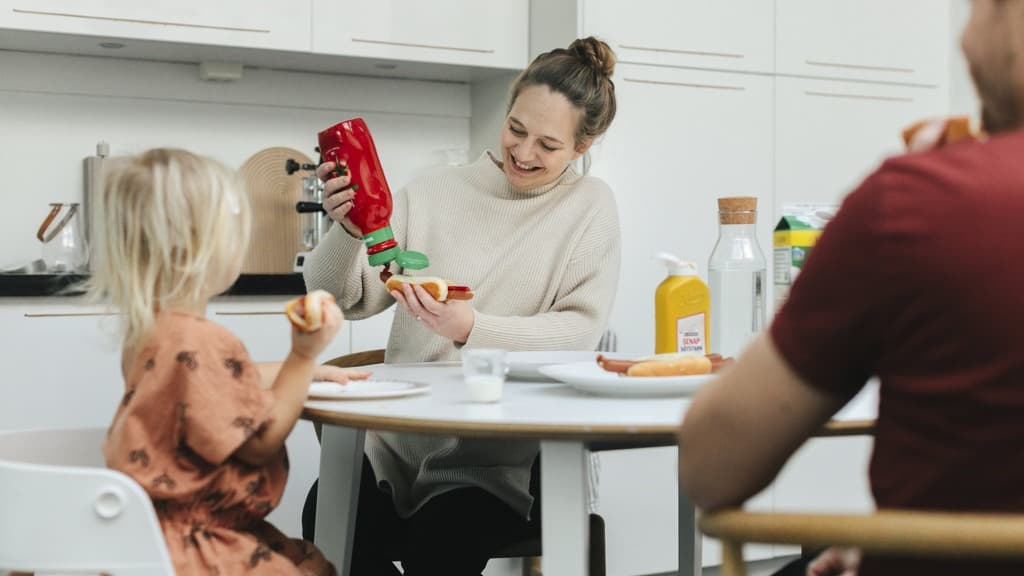 En familj äter korv med bröd vid köksbordet.