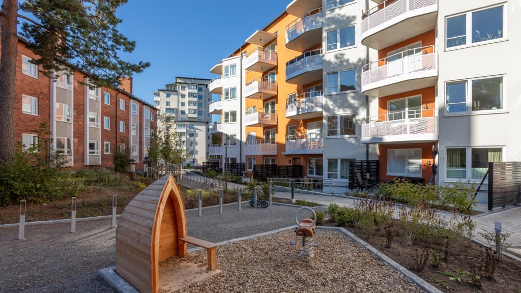 Lekplats med hus i orange fasad och vita balkonger.