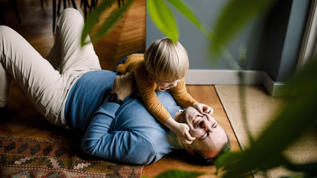 En man som ligger på golvet med ett barn på ryggen