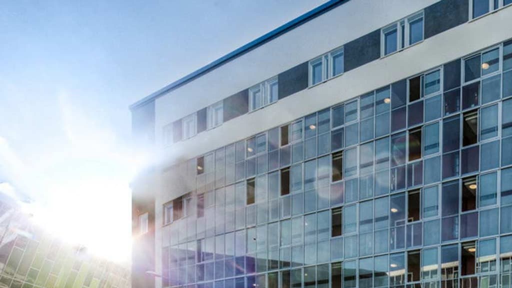 Solen mellan två hus med glasfasader. Solkatter bildas.