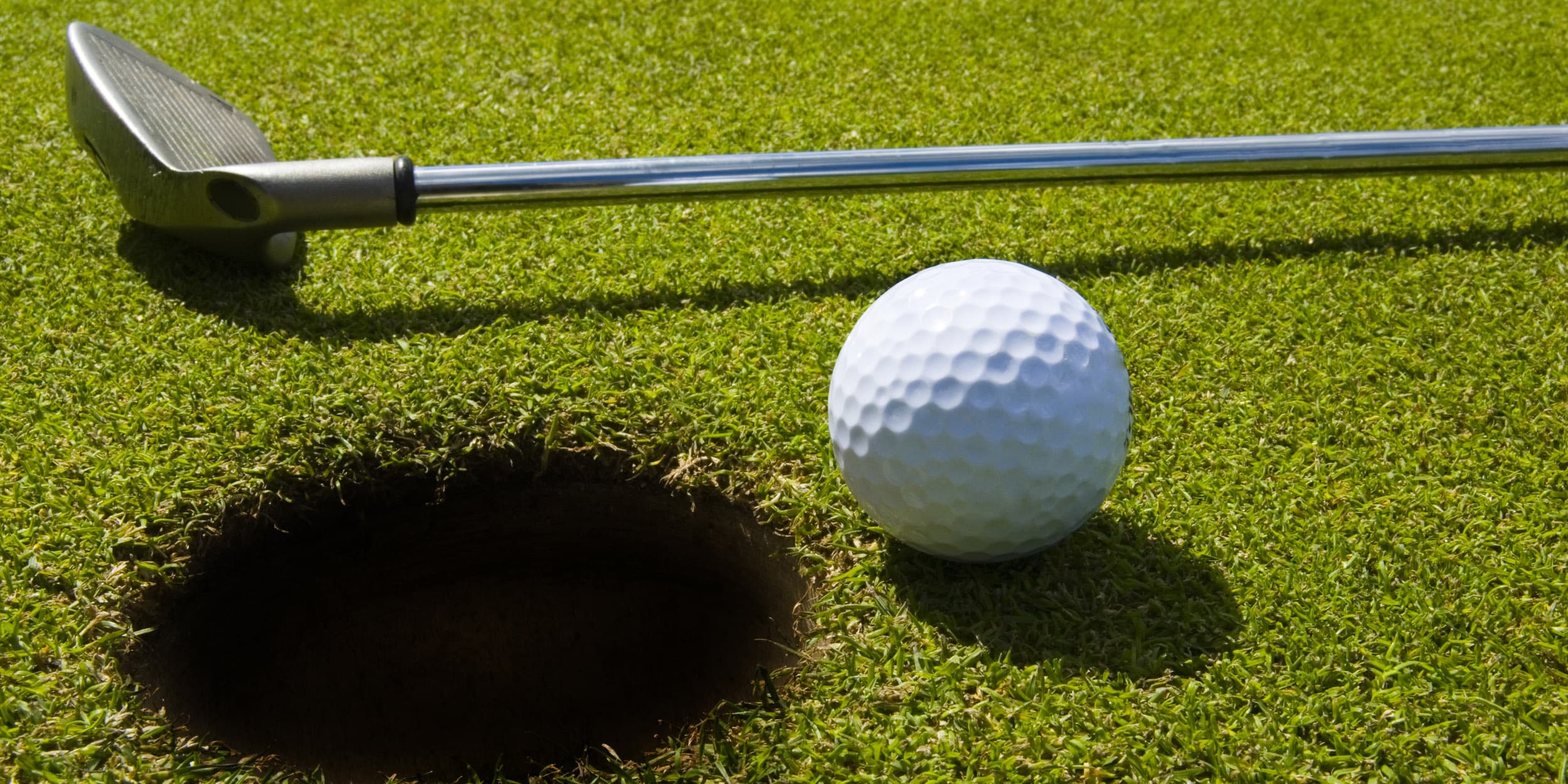 Golfboll och golklubba mot grön green