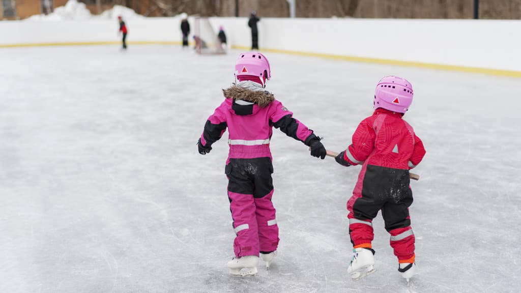 Två barn i vinteroveraller som åker skridskor på en isrink.