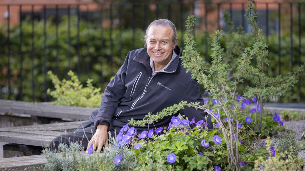 En man sitter bredvid en blomsterrabatt.