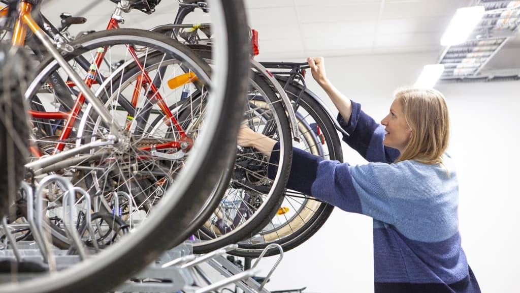 En kvinna ställer en cykel i ett cykelställ..