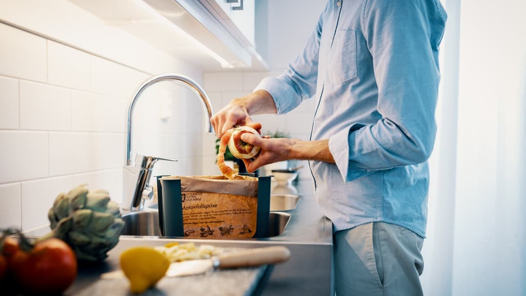 En man skalar äpple i en matavfallspåse.
