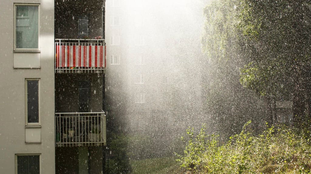 Kraftigt regn faller över en fastighet och dess gröna gård.