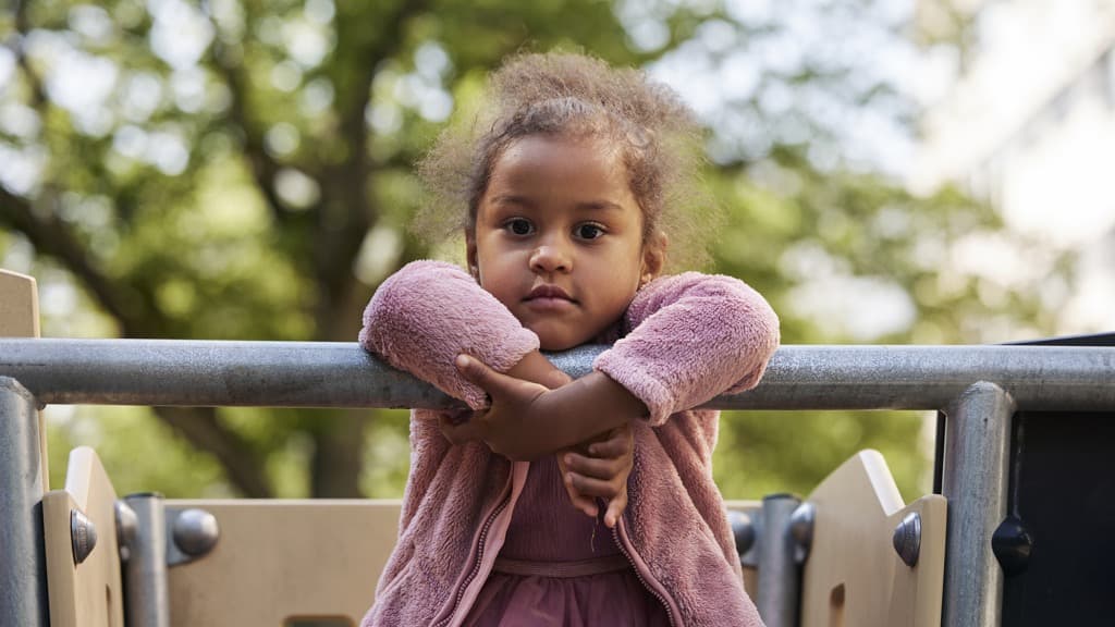 Mörkhårig flicka i rosa kläder hänger på en lekställning