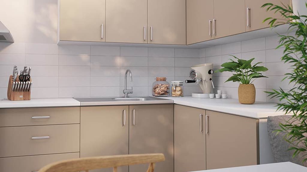 Ett ljust kök med beige skåpluckor och handtag i metall. Knivställ, kaffemaskin, grön växt och burkar med kakor på köksbänken.