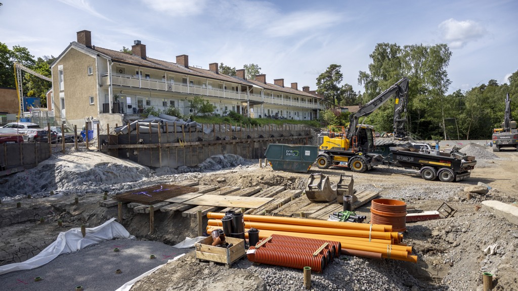 Byggarbetsplats med äldre hus i bakgrunden.