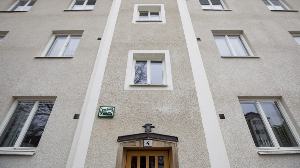 En ljusgrå husfasad i puts med träport och FB-skylt sedd lite ur grodperspektiv