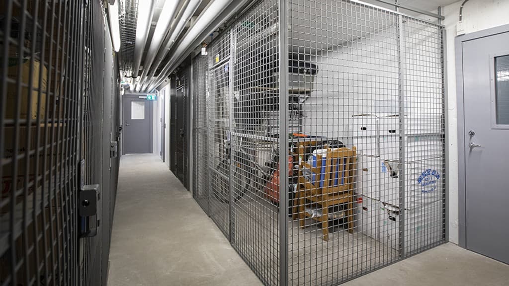 En belyst källargång med förråd på båda sidor.